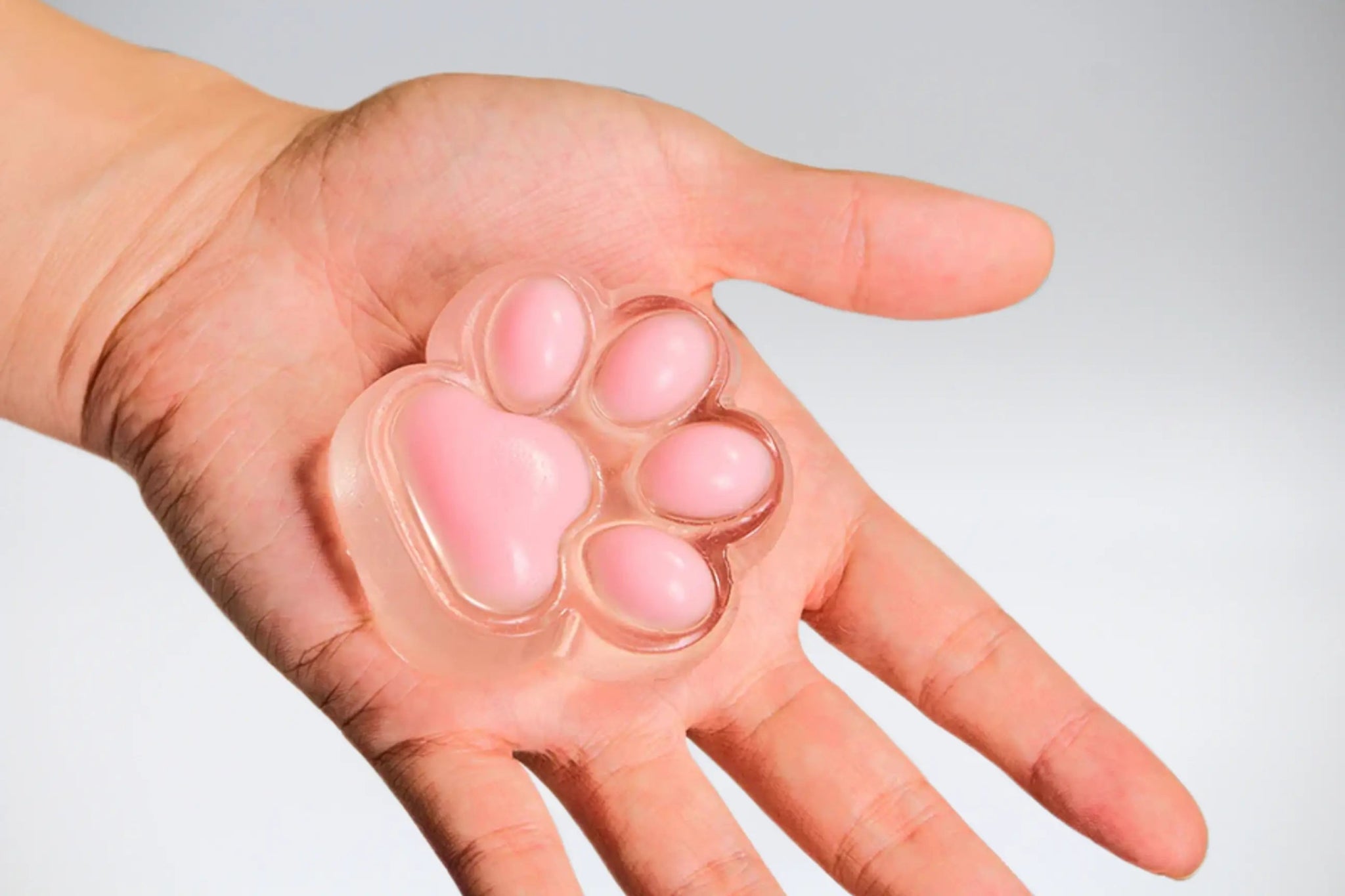 Pink Cat Paw Squishy resting in hand, soft transparent silicone toy with jelly-like beans, cute and stress-relieving.